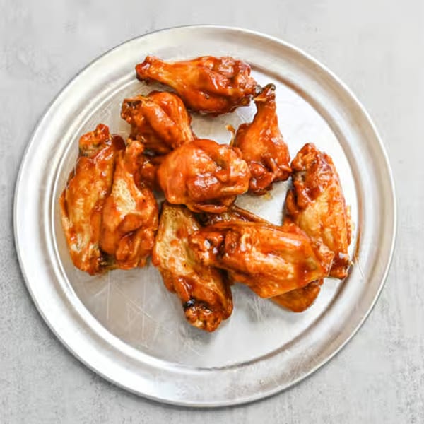 A silver platter filled with several Krave Pizza and Wings' buffalo wings, glistening with sauce.